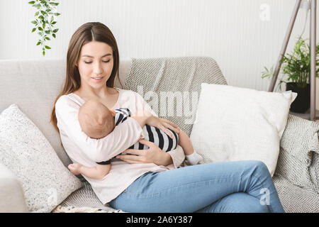 Mom holding newborn child, lulling baby on couh at home Stock Photo