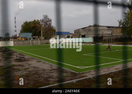 A boy plays football as a power station operates on the background. Stock Photo