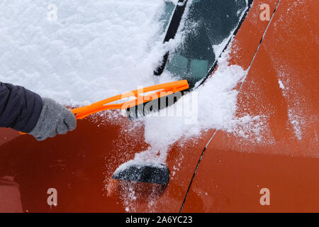 Car covered with snow. Brush in mans hand. Man in gray gloves is brushing orange car from snow. Stock Photo