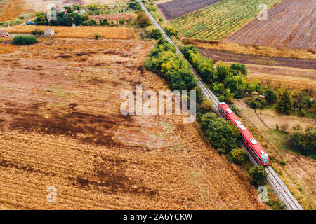 Red passenger train traveling through countryside, aerial view from drone pov in autumn afternoon Stock Photo