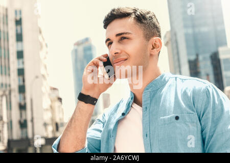 Outdoors Leisure. Stylish guy standing on the street talking on smartphone smiling joyful close-up side view Stock Photo
