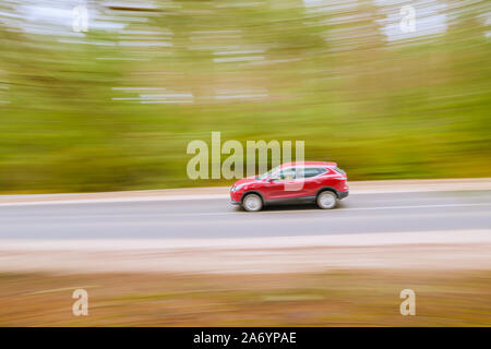 Fast moving red car on asphalt road. Panoramic shot, blurred background. Stock Photo