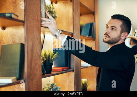 Elegant man taking book from bookshelf. Education and hobby concept Stock Photo