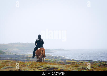 Woman riding along the water's edge on a pinto Icelandic horse in south Iceland Stock Photo
