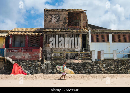 Arembepe, Brazil - Circa September 2019: Surfer passing in front of decaying houses at the beach in Arembepe Stock Photo