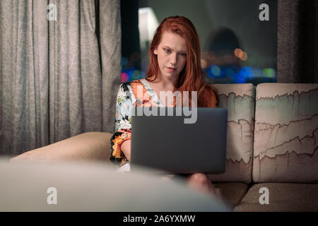 Beautiful redhead business woman working on laptop in hotel room or office space Stock Photo