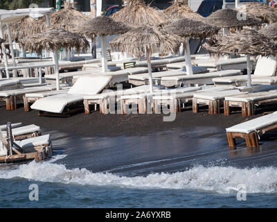 Empty white sunbeds on a black sand beach on stormy day with strong wind rough weather Santorini Stock Photo