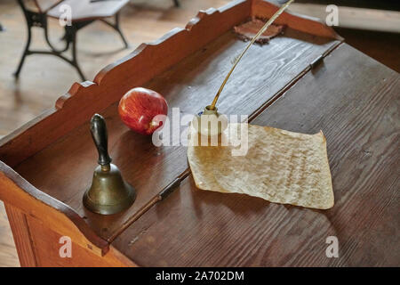 Vintage school teacher podium with an apple, a bell and a quill pen and paper in an 18th Century old schoolhouse or school classroom. Stock Photo