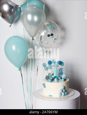 White and blue cake with candy and cookie number one on boy first birthday. Balloons and confetti on background Stock Photo