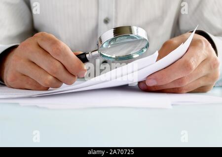 Businessman looking through a magnifying glass to documents Stock Photo