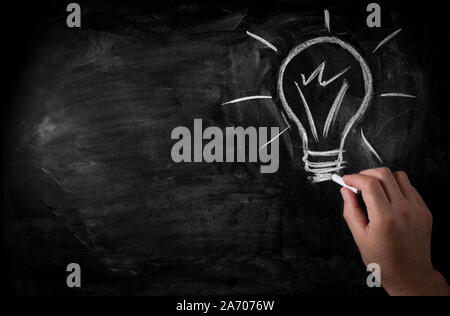 man draws a chalk lightbulb on a black school board Stock Photo