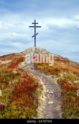 Metal cross on top of the mountain and grassy road leading to him Stock Photo