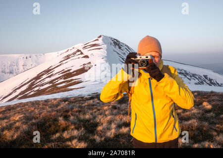 Photographer in yellow jacket taking photo on snowy winter field Stock Photo