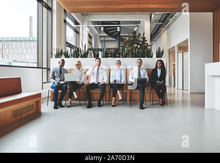 Smiling group of diverse businesspeople sitting in chairs together in an office reception waiting to be interviewed Stock Photo