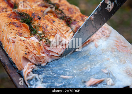A cook is cutting a piece of salmon with a knife Stock Photo