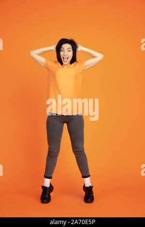 Caucasian young woman's portrait on orange studio background. Beautiful female brunette model in shirt. Concept of human emotions, facial expression, sales, ad. Copyspace. Winning, crazy happy. Stock Photo