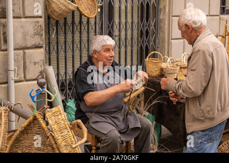 A male basket weaver at a craft market in a hilltop town in Italy talking to some customers Stock Photo