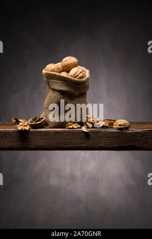 walnuts in jute bag on wooden table with dark background Stock Photo