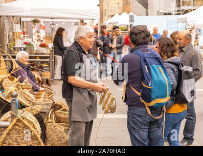 A male basket weaver at a craft market in a hilltop town in Italy talking to some customers Stock Photo