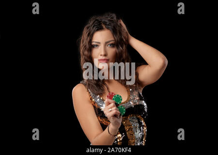 Alluring brunette female wearing in a multi-colored sequin dress. She is looking at the camera, touching her hair and holding some chips in her hand w Stock Photo