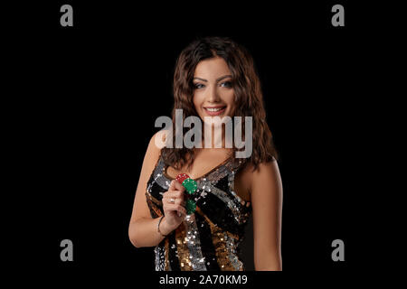 Attractive brunette lady with a curly hair, wearing in a multi-colored sequin dress. She is smiling and showing some chips in her hand while posing st Stock Photo