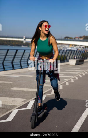 Pretty young woman riding an electric scooter in the street on a sunny day Stock Photo