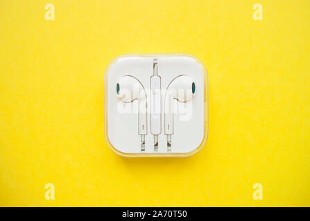Earphones in a white plastic case on a bright yellow background. Stock Photo