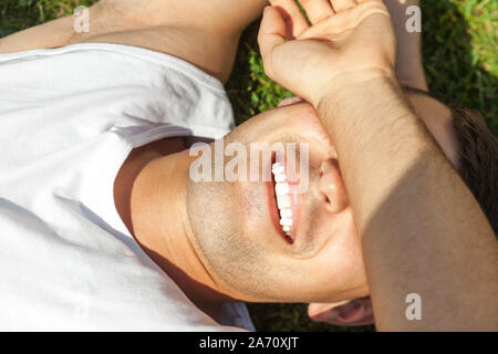 Handsome smiling man lying on the grass covering his eyes with hand against the sun Stock Photo