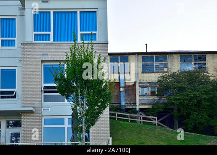 Two apartment buildings one old with broken windows and not in use another with new siding and new windows Stock Photo