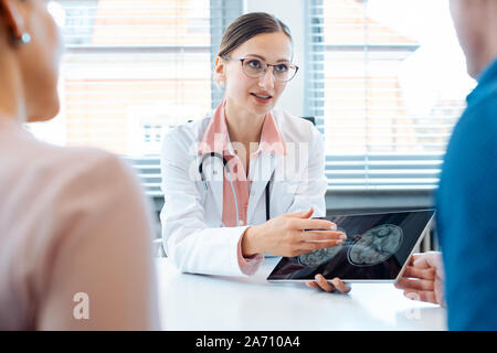 Doctor woman showing patients x-ray pictures on her tablet computer Stock Photo