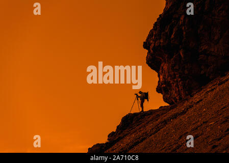 Landscape photographer in cliff face taking nature pictures of mountains with tripod at sunset in the Dolomites, South Tyrol, Italy Stock Photo