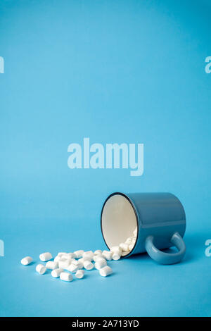 Overturned cup with marshmallows on a blue background. Cocoa drink concept. Stock Photo