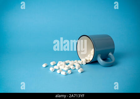 Overturned cup with marshmallows on a blue background. Cocoa drink concept. Stock Photo