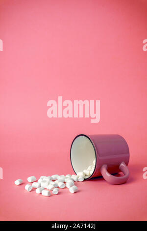 Overturned cup with marshmallows on a pink background. Cocoa drink concept. Stock Photo