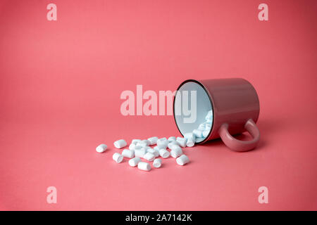 Overturned cup with marshmallows on a pink background. Cocoa drink concept. Stock Photo