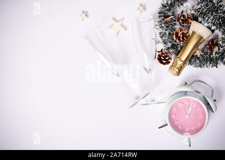 Christmas or New Year composition. Champagne bottle with two glasses, decoration and a clock showing almost midnight, on white background. Copy space. Stock Photo