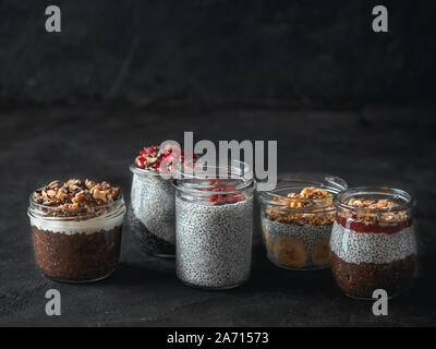 Set of chia pudding in different glass jars on dark table. Assortment of chia puding with different fruits, nuts,ingredients. Copy space for text. Superfood,detox,healthy overnight breakfast concept Stock Photo