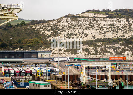 Lorries queue in several lanes for customs clearance at the ferry port of Dover, England, beneath a harbour crane in the foreground. The town's White Cliffs rise in the background. Little room remains to manoeuvre in the cramped harbour area when traffic comes to a standstill during checks. Stock Photo