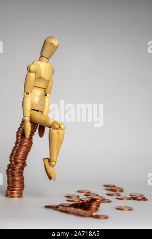 wooden doll counting money sitting on a stack of cent coins the rest scattered on the floor Stock Photo