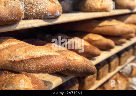 Bread variety on wooden shelves. Freshly baked loaves on bakery racks. Bread diversity. Baked goods and bakery context. Stock Photo