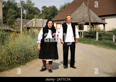 Local Maramures senior couple walking towards church in Sunday's best clothing in Breb, Romania. Lady holding roses in hand Stock Photo