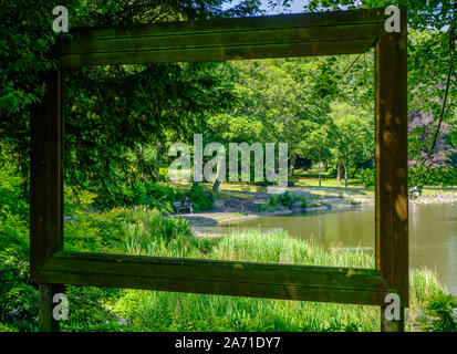 Newcastle, United Kingdom -July 1, 2019: View through large hollow picture frame of a pond, trees and a man sitting on a bench at Leases Park in Newca Stock Photo