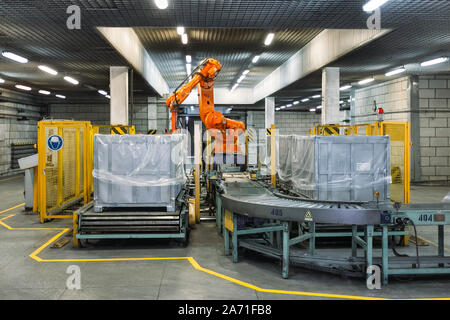 Robot Hand manipulator packaging factory products from conveyor into container. Stock Photo