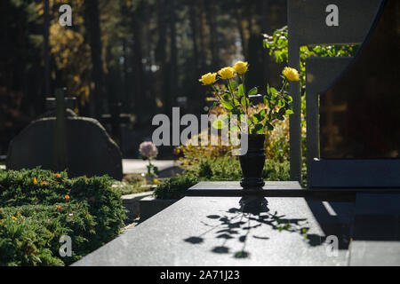 Tombs before the day of the dead are decorated with flowers in Vilnius, Lithuania. Yellow roses in a vase and their shadows, tombstones with crosses Stock Photo