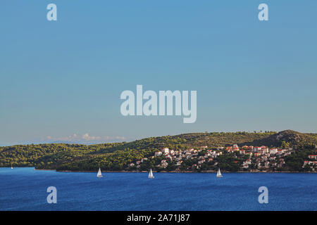 Three boats sailing in front of a small beautiful city built on an island in the sea on a sunny warm summer day Stock Photo