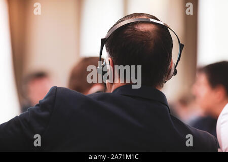Shallow depth of field (selective focus) image with a man sitting on a chair and listening to a conference and having headphones with translation on h Stock Photo