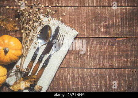 Thanksgiving or autumn table decoration with cutlery and linen napkin on rustic wooden background. Top view with space for text on right side. Stock Photo