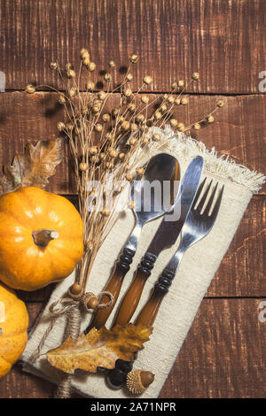 Thanksgiving or autumn table decoration with cutlery and linen napkin on rustic wooden background. Top view, vertical photo. Stock Photo