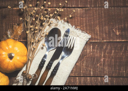 Thanksgiving or autumn table decoration with cutlery and linen napkin on rustic wooden background. Top view with space for text on right side. Stock Photo