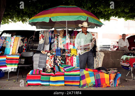 Mexican vendor reading newspaper at his market stall selling colourful textiles at Mercado Hidalgo. Guanajuato, Mexico. Jun 2019 Stock Photo
